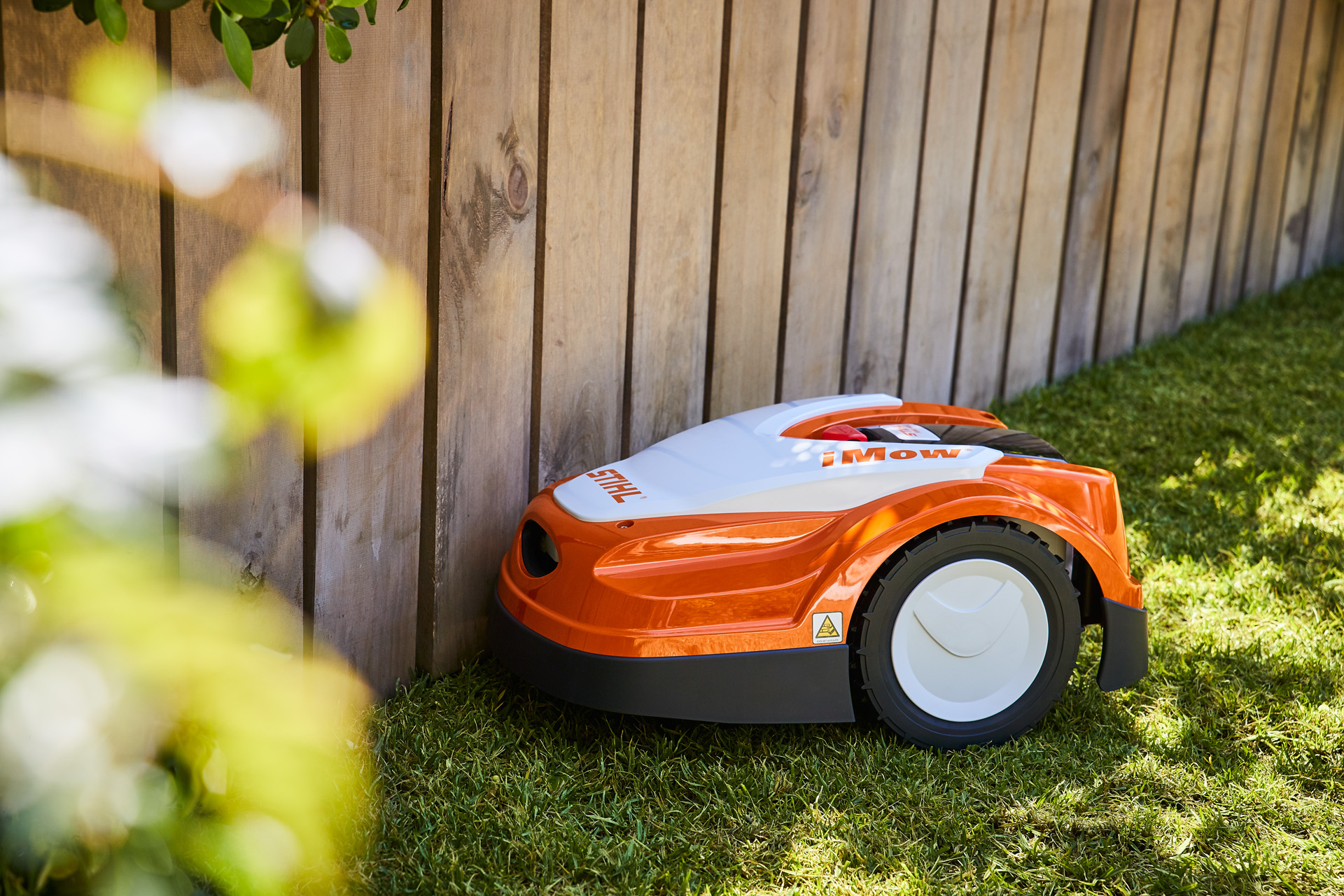 Ένα χλοοκοπτικό ρομπότ iMow® στέκεται μπροστά από φράχτη κήπου